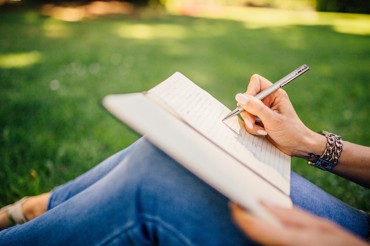 woman sitting outdoors, writing in a journal.